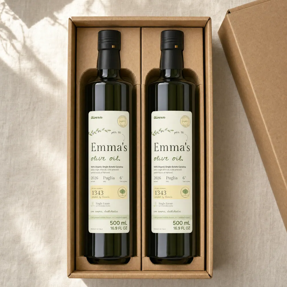 Two Oliverse bottles, both labelled "Emma's olive oil", lying side by side in the cardboard inserts of an open kraft gift box